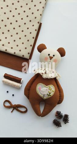 Overhead still life of brown plush bear beside fabrics, ribbon, thread, scissors and pinecones, warm rustic feel Stock Photo
