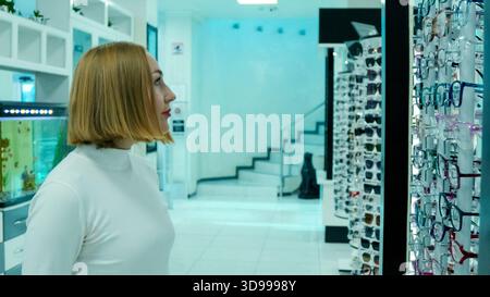 Rear view of a female optician standing in front of a well-stocked glasses Stock Photo