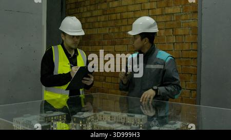 Two construction workers in yellow vests discussing plans at an outdoor site Stock Photo