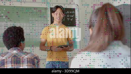 Presenting Asian teen male wearing yellow T-shirt, jeans holding tablet, speaking at front of class Stock Photo