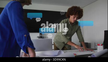 Leaning man in olive shirt pointing to plans in meeting room, woman in blue blazer observing Stock Photo