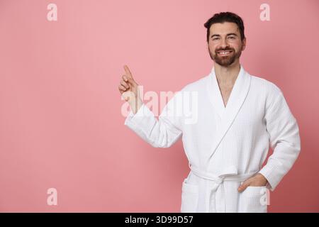 Man in bathrobe pointing at something on pink background. Space for text Stock Photo