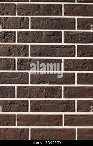 A wall made of dark bricks arranged in a consistent pattern. The white grout lines create contrast against the bricks. The surface appears smooth and Stock Photo