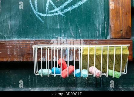Close-up of a traditional school chalkboard with colorful chalk pieces and a sponge in a metal tray. Stock Photo
