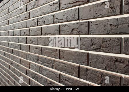 A close look at a wall made of dark bricks shows clear patterns and textures. The thin white grout lines stand out against the dark surface, creating Stock Photo