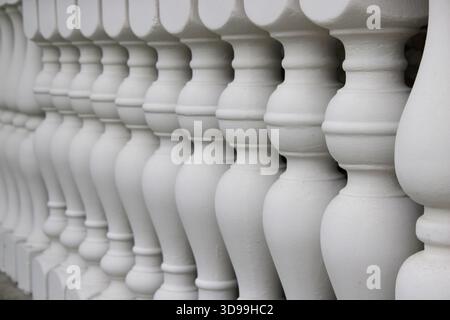The scene showcases a series of white balusters lined up in a row. Each baluster has a rounded shape, forming a continuous line along a railing or str Stock Photo