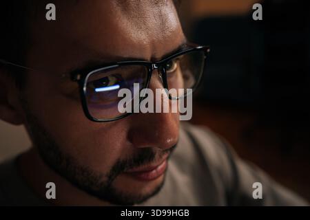 Close-up face of serious software developer wearing glasses, focused looking on computer screen reflecting in lenses while working late into night Stock Photo