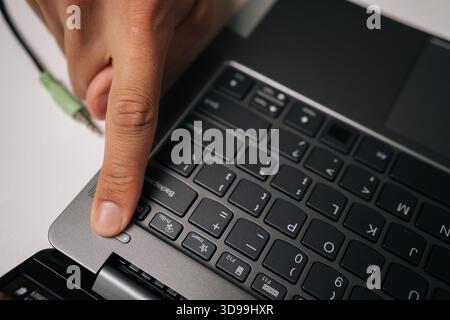 Close-up view of male finger pressing power button on laptop keyboard sitting at table, initiating journey of productivity or gaming excitement in Stock Photo