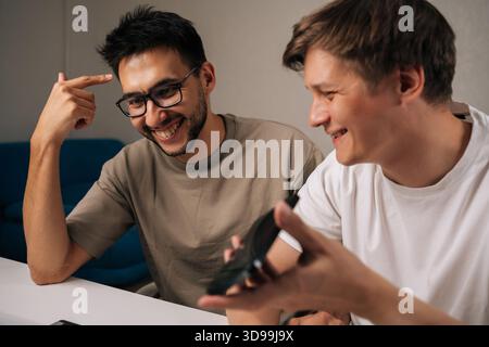 Positive young men in office collaborating on startup plan, using smartphone for calls and messages, sharing ideas, planning strategy and driving Stock Photo