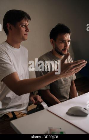 Vertical portrait of serious young men intently collaborating on computer, developing anew startup project, working late in intimate office setting Stock Photo