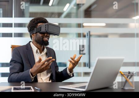 African american businessman wearing a virtual reality headset and gesturing while interacting with a digital world during a technology meeting in a modern office environment Stock Photo