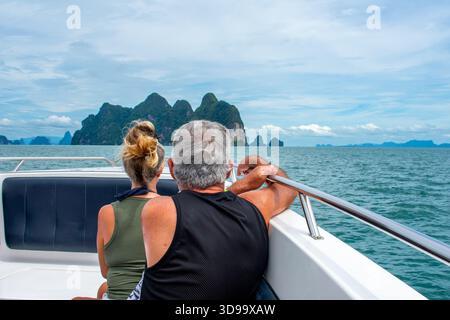 Happy couple sitting on a boat together on holiday in Phuket, Thailand. Man and woman looking at island from yacht in Phi Phi Islands Stock Photo