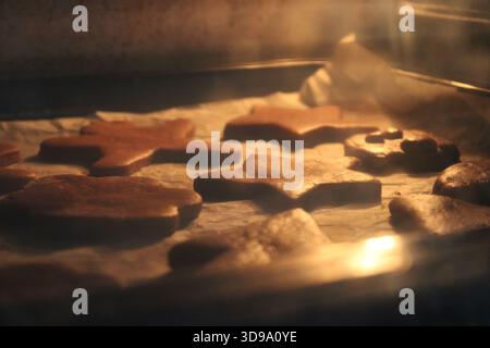 Cookies are placed on a baking tray inside an oven. Different shapes are visible in the warm glow. The baking process creates a familiar scene during Stock Photo