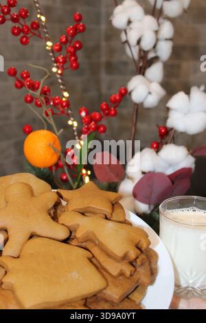 Cookies are placed on a plate with a glass of milk nearby. Winter decorations include red berries and cotton branches. The scene is set for a holiday Stock Photo