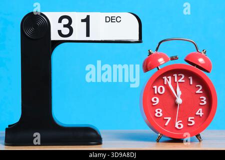 Red alarm clock on blue background and calendar with date December 31 Stock Photo