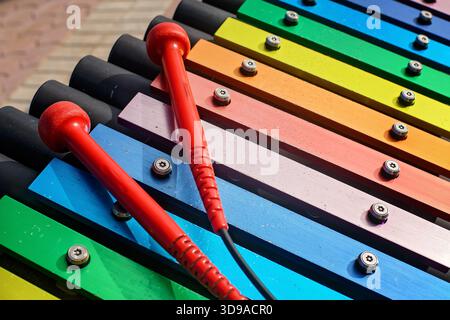 A vibrant close-up of a colorful outdoor xylophone with two  red mallets resting on the rainbow-colored keys in a public park Stock Photo