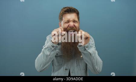 Man wearing denim jacket with beard and clenched fists performs a mocking crying gesture in studio; humor. Stock Photo