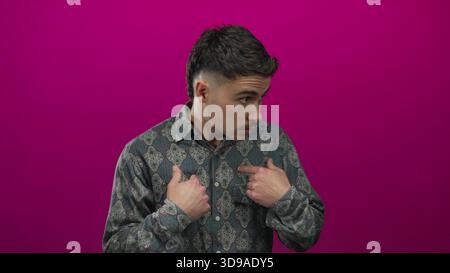Young hispanic man surprised and pointing at himself against a vibrant pink background, highlighting expression and emotion. Stock Photo