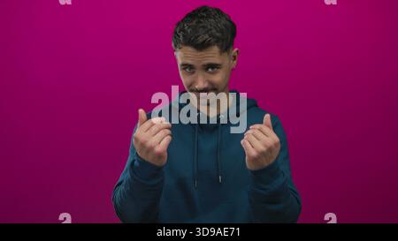Young hispanic man gestures come here with hands against a vibrant pink background, appearing inviting and playful in a vivid, isolated studio shot. Stock Photo