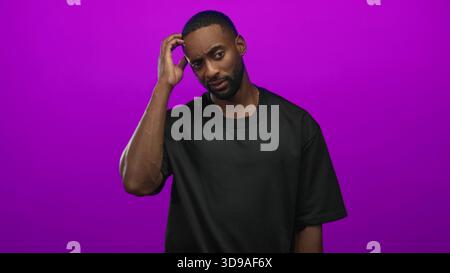 Man scratching head and touching temple with right hand in purple studio, wearing black t shirt and gold chain; confusion doubt puzzlement. Stock Photo