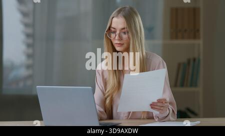 Caucasian concentrated business woman working with laptop checking papers in office focused businesswoman girl female entrepreneur indoors reading Stock Photo