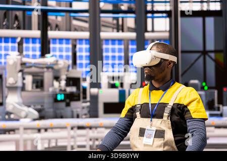African american technician in smart manufacturing plant using VR for industrial training. Industry 4.0 engineer immersed in augmented reality, enhancing operational efficiency in automated factory. Stock Photo