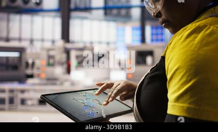 Close up of technician using tablet CAD app to design smart factory layouts. Specialist using simulation application on device to simulate and optimize production systems in automated plant, camera A Stock Photo