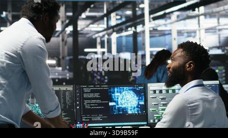 Server hub manager checking AI generated data analytics graphs, congratulating worker. Data center team leader doing fist bump with admin using artificial intelligence showing system metrics, camera B Stock Photo