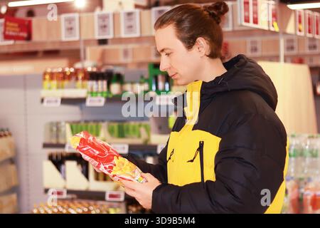 Young man reading label on frozen french fries package in supermarket aisle, checking ingredients. High quality photo Stock Photo