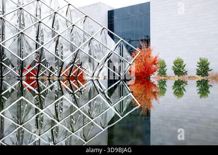 Delta Solar Sculpture National Air And Space Museum Washington DC | WASHINGTON D.C., United States — A close view of Delta Solar's stainless steel lattice shows its triangular sails doubled by reflection, with a fiery maple tree and the National Air and Space Museum's dark glass wall behind. Alejandro Otero built the sculpture from an open delta-shaped grid holding sixty-four sails that rotate independently in the wind. It was dedicated in 1977 as Venezuela's Bicentennial gift to the United States. Stock Photo