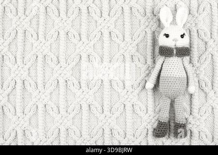 Demonstrating the colors of 2026 - Cloud Dancer. Knitted children's toy bunny on a knitted white cloth. Color concept. Stock Photo