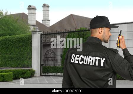 Security guard using radio near house outdoors. Private property protection Stock Photo