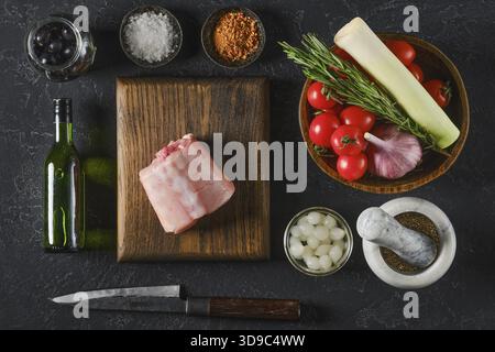 Fresh ingredients are beautifully arranged on a wooden board, including a piece of raw rabbit saddle meat, ripe tomatoes, garlic, leeks, olives, and h Stock Photo