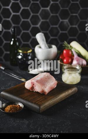 A raw rabbit saddle loin on a wooden cutting board in a kitchen setting. Fresh vegetables and spices surround it, providing a vibrant backdrop. The sc Stock Photo
