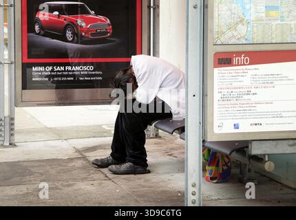 San Francisco, California, USA - August 15, 2013: Homeless man sleeping on a bench at a bus stop in San Francisco Stock Photo