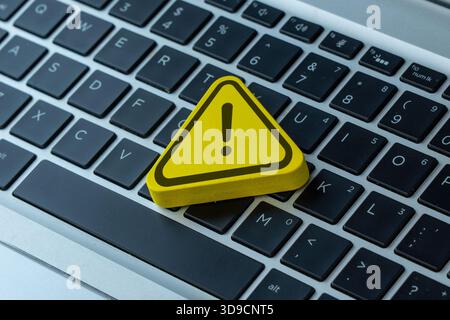 A yellow warning sign with an exclamation mark placed on a laptop. Cybersecurity, computer error, system alert, online danger concept. Stock Photo