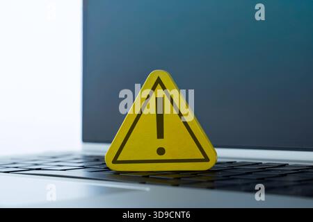 A yellow warning sign with an exclamation mark placed on a laptop. Cybersecurity, computer error, system alert, online danger concept. Stock Photo