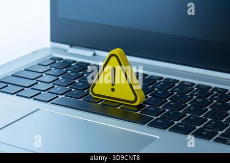 A yellow warning sign with an exclamation mark placed on a laptop. Cybersecurity, computer error, system alert, online danger concept. Stock Photo