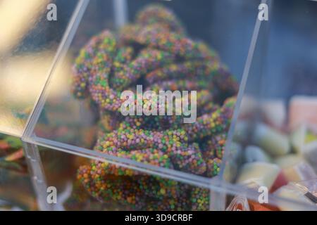 Joyful close up view of colorful gummy candy worm with sweet sugar sprinkle in transparent bin. This fun, delicious dessert snack treat for sale in ca Stock Photo