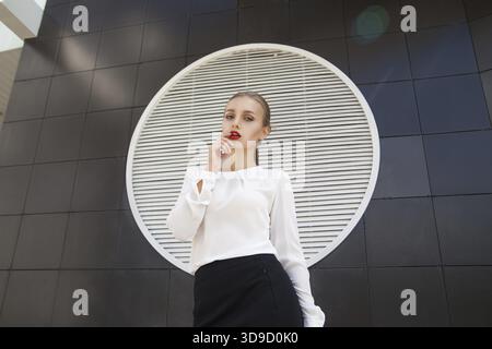Beautiful blonde businesswoman with red lips against of building wall Stock Photo