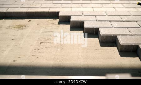 Construction worker carefully placing gray paving stones in a row on sand, creating a new pavement Stock Photo