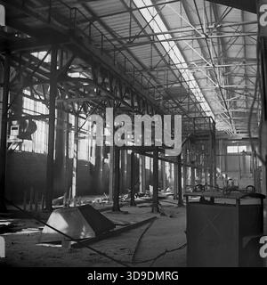Sloviansk, Ukraine, USSR, 1960s. An archival interior view of a workshop under construction at the Armaturno-Izolyatorny Zavod (AIZ). The vast industrial hall features high steel truss ceilings with skylights and heavy vertical support beams. The floor is scattered with construction debris and raw materials. This atmospheric image captures the expansion of industrial capacity and the scale of engineering works in the peaceful Donbas region during the Soviet era. Stock Photo