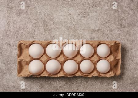 top view of ten fresh white eggs in cardboard carton textured gray stone background, copy space for text, healthy protein and breakfast concept Stock Photo