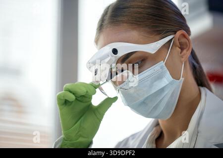 Young Adult Caucasian Woman Examining Sample Using Magnifying Glass in Laboratory Stock Photo