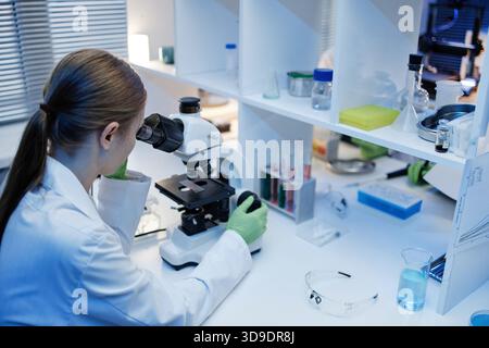 Young Adult Caucasian Woman Examining Samples under Microscope in Laboratory Stock Photo