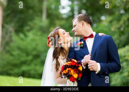 Bride and groom dressed in elegant wedding attire lean toward each other and share a gentle kiss, the bride holding a vibrant bouquet — capturing love Stock Photo