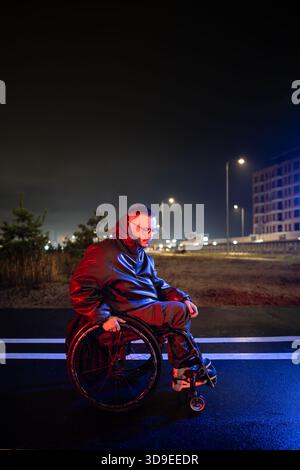 Upset young disabled man in wheelchair in rgb neon light deeply thinking, dealing with stress. Stock Photo