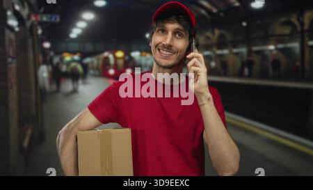 Man holds cardboard box with one arm and talks on phone at train station; efficiency reliability service. Stock Photo
