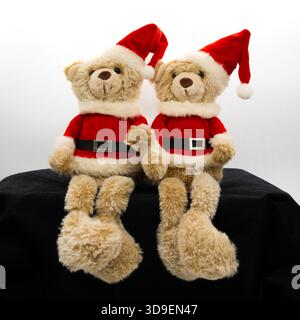 Two small Christmas teddy bears wearing Christmas bobble hats and Santa styled tunics with a black belt and silver buckle. Stock Photo