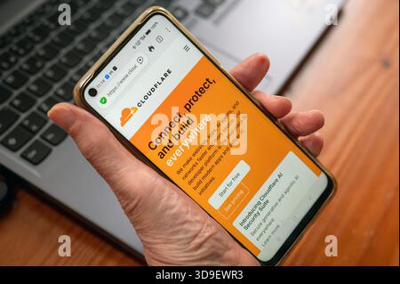 Madrid, Spain - December 5, 2025: A hand holds a smartphone displaying Cloudflare’s orange landing page about connect, protect, and build everywhere, Stock Photo